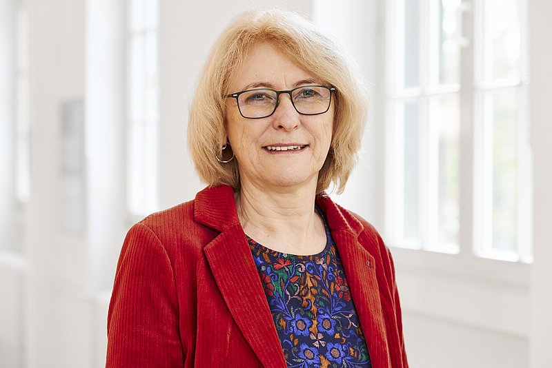 Porträt einer Frau mit blondem Haar, Brille und rotem Blazer